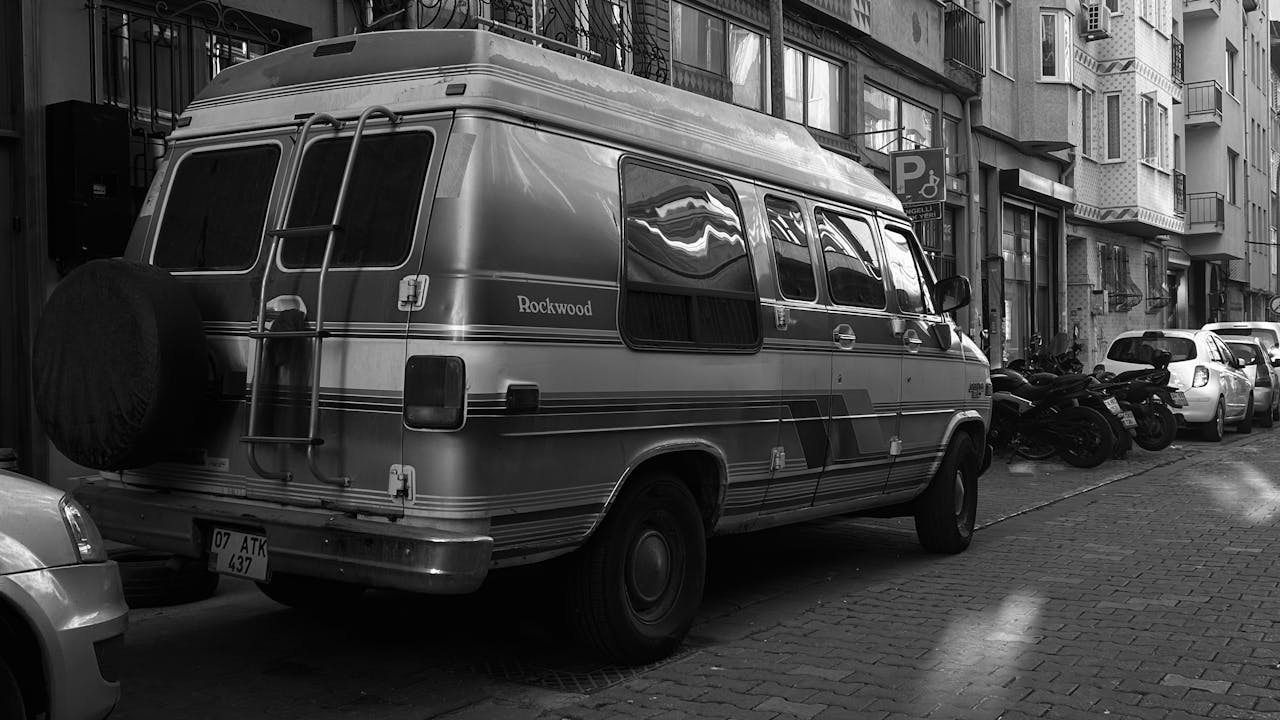 Black and white photo of a vintage van parked on a city street, emphasizing urban life.